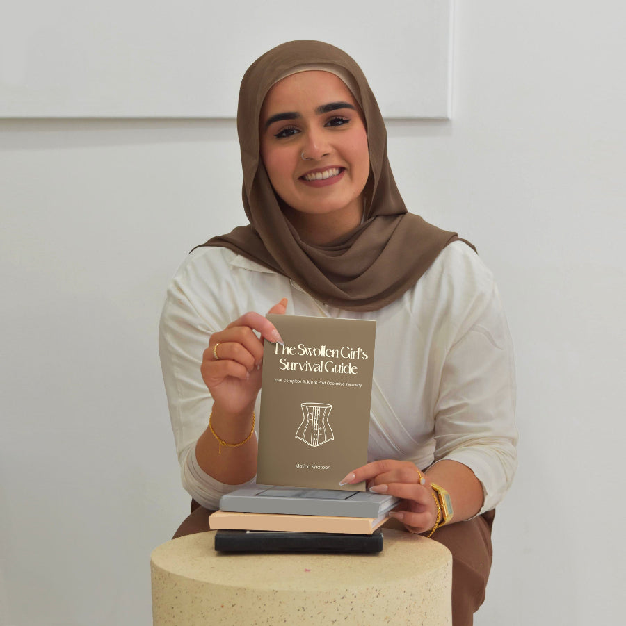 Woman holding a book titled 'The Swollen Girl's Survival Guide' against a plain background